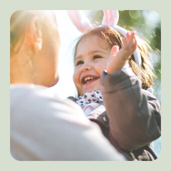 Zwei Personen im Sonnenlicht im Freien, wobei ein Kind Hasenohren trägt und frühlingshafte Osterstimmung entsteht.