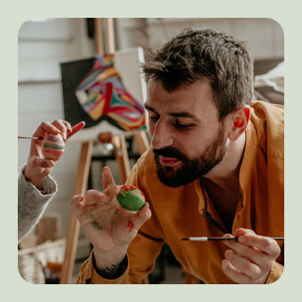 Personen bemalen bunte Ostereier in einer kreativen Oster‑Bastelszene mit Pinseln und Farben.