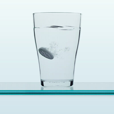Ein Wasserglas mit auflösender Brausetablette vor hellem Hintergrund.