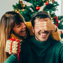 Zwei Personen in festlicher Umgebung, eine mit Rentiergeweih-Stirnband, Weihnachtsdeko und Geschenk mit roter Schleife.
