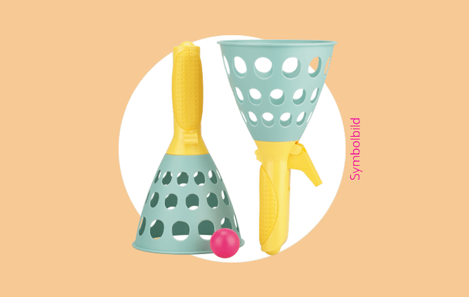 Zwei bunte Fangbecher mit Löchern und einem pinken Ball auf orangefarbenem Hintergrund als Symbolbild.