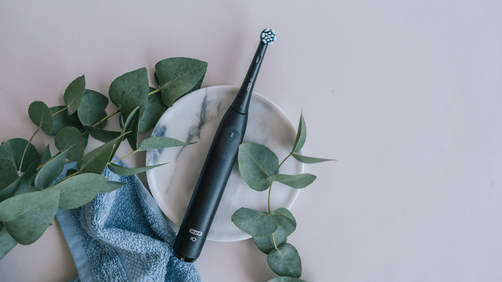 Schwarze elektrische Zahnbürste auf Marmor mit Eukalyptus & Handtuch – stilvolle & moderne Zahnpflege.