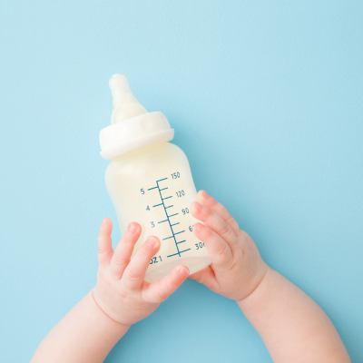 Ein Babyfläschchen gehalten von Babyhänden auf blauem Hintergrund.