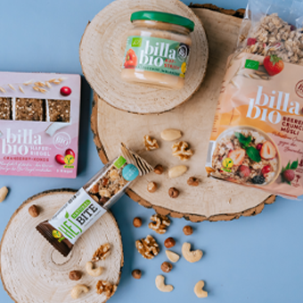 Bio Produkte wie Granola, Nussmus, Fruchtriegel und Snacks auf Holzscheiben mit Nüssen vor blauem Hintergrund. Link zur Kategorie Ernährung.