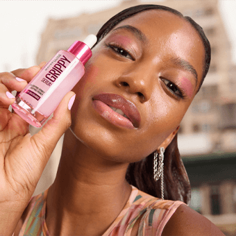 Person hält GRIPPY Make-up Primer vor Gesicht – urbaner Hintergrund, vegane Kosmetik, Primer für langanhaltendes Make-up. - Link zum Grippy Serum