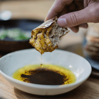 Hand tunkt Brot in Olivenöl-Balsamico-Schale – mediterraner Genuss, Food-Fotografie.