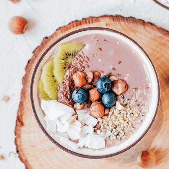 Smoothie-Bowl mit Kiwi, Blaubeeren, Haselnüssen, Kokosflocken und Samen auf Holzbrett – gesunde Frühstücksidee.