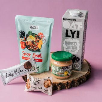 Gesunde Food-Produkte wie Shape Republic Bowl, Oatly Barista, Koro Energy Ball & Billa Bio Erdnussbutter auf Holzplatte