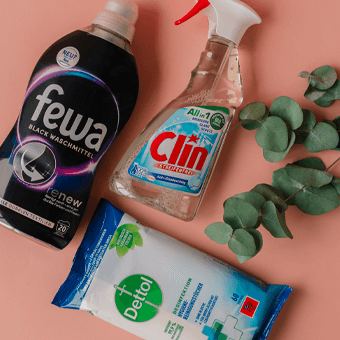 Fewa Waschmittel, Clin Reiniger und Dettol Desinfektionstücher auf rosa Hintergrund.