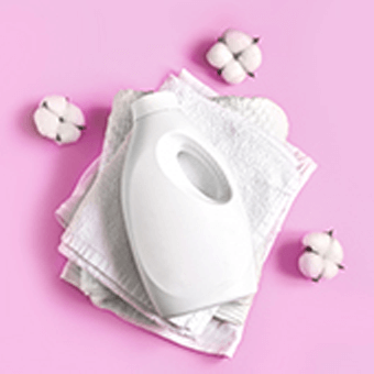 Weiße Waschmittelflasche und weiße Handtücher auf rosa Hintergrund.