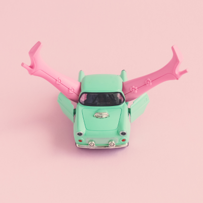 türkises Spielzeugauto aus dem pinke Stiefel herausragen, Hintergrund in rosa