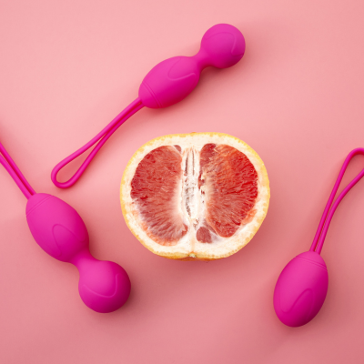 Sexspielzeug für Frauen platziert um eine Grapefruit auf rosa Hintergrund