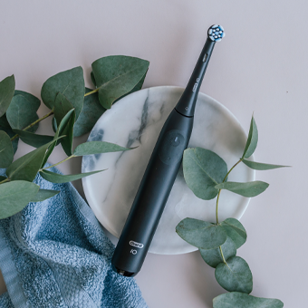 Schwarze elektrische Zahnbürste auf Marmorteller mit Eukalyptus und Handtuch – moderne Zahnpflege mit Oral-B