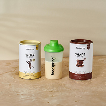 Foodspring Shape Shake Schoko, Whey Protein Vanille & Shaker mit Pulver – Fitnessprodukte auf Marmorfläche. Link zu allen Proteinpulvern von Foodspring.