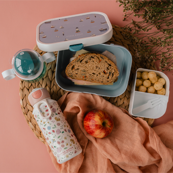 Lunchbox mit Brot, Snackbox mit Bällchen, Trinkflasche & Apfel auf rosa Hintergrund – gesunde Jause für Kinder.