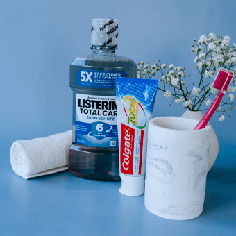 Mundpflege-Set mit Listerine, Colgate Zahnpasta & Zahnbürste im Becher vor blauer Wand – tägliche Zahnhygiene entdecken.