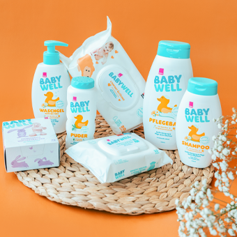 Baby Well Pflegeprodukte – Shampoo, Lotion, Wundschutz & Feuchttücher auf Matte vor orangefarbenem Hintergrund.