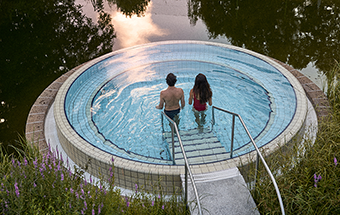 Zwei Personen im runden Pool mit Treppe, umgeben von Natur und spiegelndem Wasser – entspannte Auszei