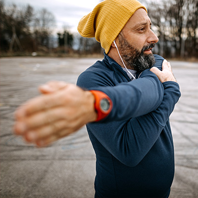 Person in blauer Jacke und gelber Mütze streckt draußen den Arm, trägt eine rote Uhr am Handgelenk