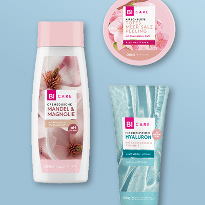 BI CARE Pflegeprodukte: Duschgel mit Mandel & Magnolie, Meersalz-Peeling & Aloe-Vera-Creme auf blauem Hintergrund.