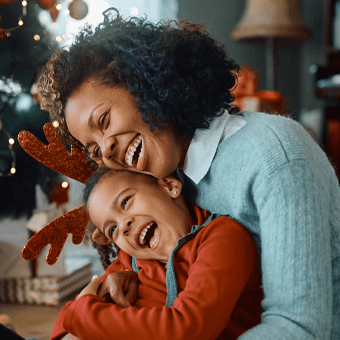 Zwei Personen in festlicher Umgebung, eine mit Rentiergeweih-Stirnband, Weihnachtsdeko im Hintergrund.