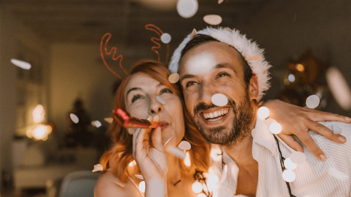 Zwei Personen mit festlicher Deko im Hintergrund, weiße Mütze und Pullover – stimmungsvolles Winter- oder Partyfoto