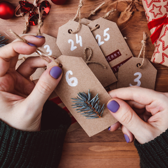 BIPA Adventskalender 2025: Geschenkanhänger in Händen, Weihnachtsdeko im Hintergrund – jetzt Vorfreude shoppen!