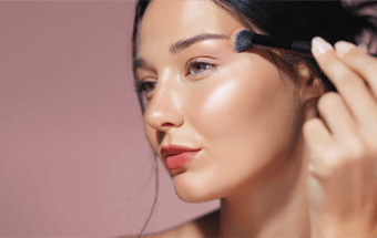 Zeigt eine Frau die sich gerade Highlighter mit einem Pinsel aufträgt - Link zu Blogartikel Highlighter auftragen