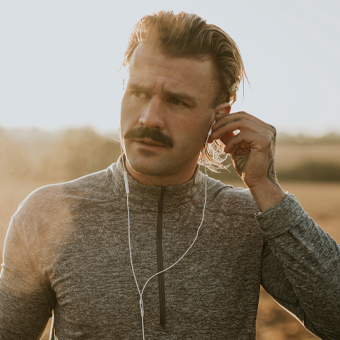 Person joggt auf einem Feldweg bei Sonnenuntergang und trägt graues Langarmshirt sowie weiße Ohrhörer.