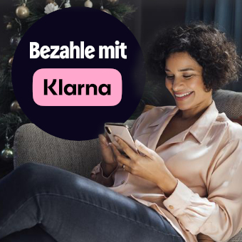Person sitzt entspannt vor Weihnachtsbaum und bezahlt online mit Klarna per Smartphone.