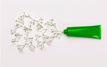 Grüne Tube mit herausströmenden Blumen – Symbol für natürliche Inhaltsstoffe in nachhaltiger Kosmetik