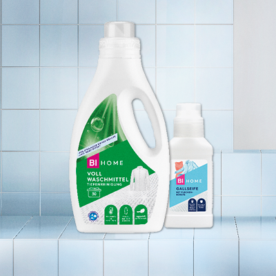 Zwei Waschmittel-Flaschen auf Fliesen: große Flasche mit grünem Etikett, kleine mit blauem – für saubere Wäsche.