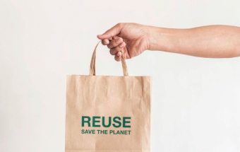 Hand hält Papiertüte mit Aufschrift ‚REUSE SAVE THE PLANET‘ – BIPA-Initiative zur Plastikvermeidung und Nachhaltigkeit