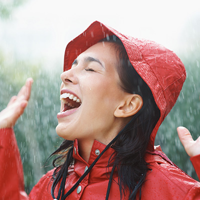 Person in roter Regenjacke mit Kapuze steht im Regen, hebt die Arme,