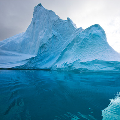 Großer Eisberg im Ozean, teils unter Wasser sichtbar, mit blauem Himmel und Wolken im Hintergrund