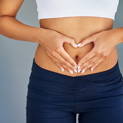 Frau in Sportkleidung formt mit Händen ein Herz über dem Bauch, Symbol für Fitness und gesunde Ernährung.