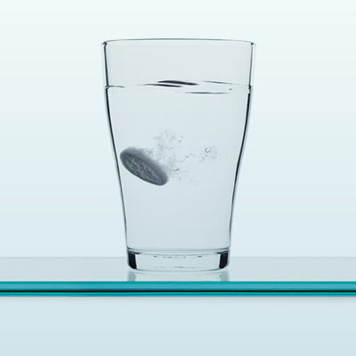 Ein Wasserglas mit auflösender Brausetablette vor hellem Hintergrund.