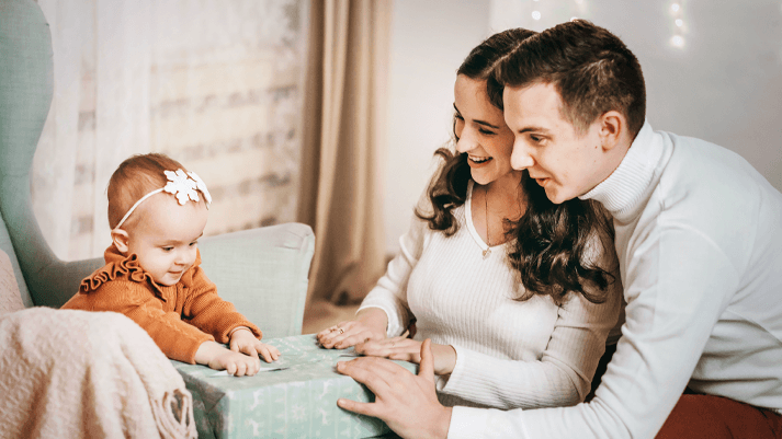 Baby sitzt auf Stuhl zwischen zwei Erwachsenen in gemütlichem Wohnzimmer – Familienfoto, Eltern-Kind-Moment