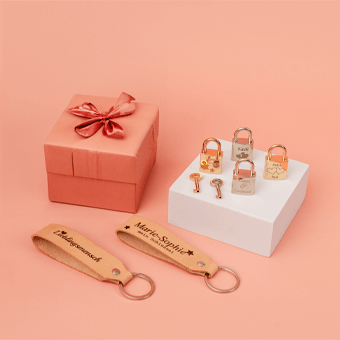 Personalisierte Geschenke: gravierte Vorhängeschlösser, Schlüssel & Lederanhänger mit Geschenkbox auf Pfirsich-Hintergrund