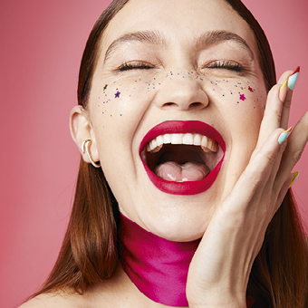 Porträt einer Person mit pinkem Halstuch vor rosa Hintergrund, unscharf – Text ‚NEU‘ unten eingeblendet. Link zur Markenseite/Neu Produkte