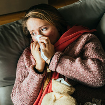 Person liegt krank auf dem Sofa, hält ein Taschentuch und trägt warme Kleidung – Tipps zur Erkältung und Immunsystem stärken.