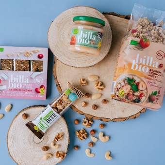 BILLA Bio Müsliriegel, Nussmix, Fruchtmüsli und Apfelmus auf Holzuntergrund – gesunde Snacks und Bio-Lebensmittel.