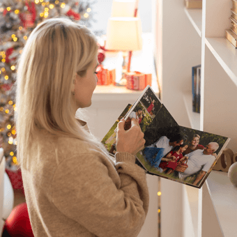 Frau blättert in Fotoalbum in festlich dekoriertem Raum, geschmückter Weihnachtsbaum im Hintergrund.