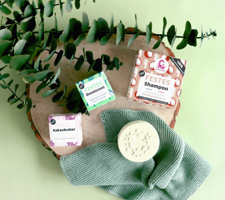 Lamazuna Naturkosmetik – feste Pflegeprodukte in umweltfreundlicher Verpackung auf Holz mit Blättern.