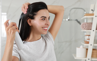 Person sprüht Trockenshampoo auf dunkles Haar im Badezimmer, Fokus auf Haarpflege und Styling für frisches Volumen.