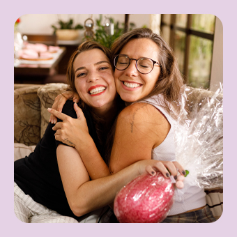 Zwei Personen sitzen gemeinsam auf dem Sofa und halten ein eingepacktes Geschenk in pinker Folie, festliche Oster‑Atmosphäre.