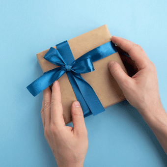 Hände binden blaue Schleife um Geschenkbox – kreative Geschenkideen für jeden Anlass entdecken.