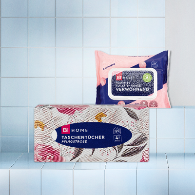 Taschentücher & Feuchttücher auf Fliesen – rosa Packung & florales Design, ideal für Hygiene & Pflege unterwegs.
