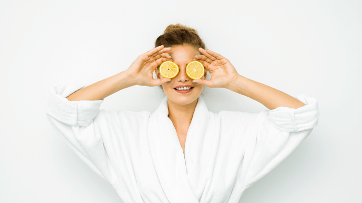 Person im weißen Bademantel hält Zitronenscheiben vor die Augen, Wellness und Frische.