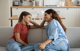 Mutter und Tochter sitzen gegenüber und lächeln sich an. Copyright: Getty Images